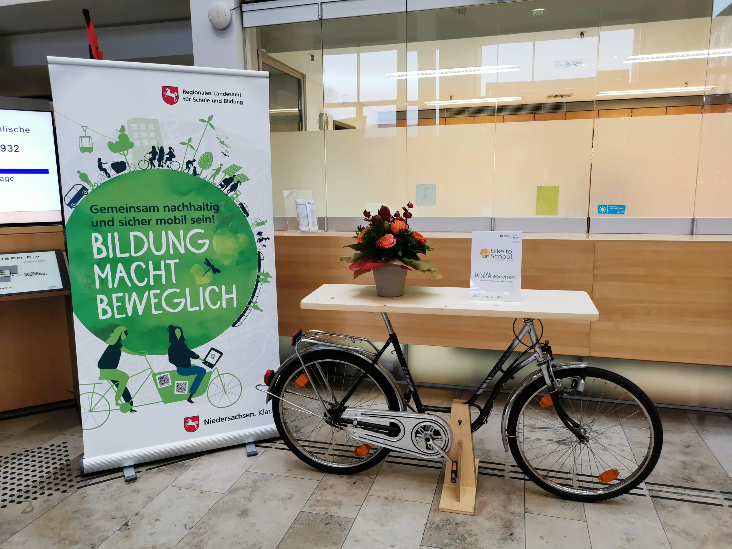 Ein zum Tisch umgebautes Fahrrad als Empfangstresen für Bike To School steht neben einem Aufsteller mit dem Slogan "Bildung macht beweglich".